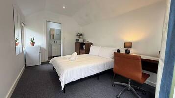 A hotel room with a bed, a desk, a chair, a small kitchenette, and a bathroom.