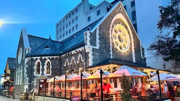 A historic building with a clock tower, outdoor seating with umbrellas, and a signboard. - Inner City Apartment - Prime location! (Christchurch)