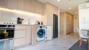 A modern kitchen with built-in appliances, a washing machine, and a dining area with a chair. - Inner City Apartment - Prime location! (Christchurch)