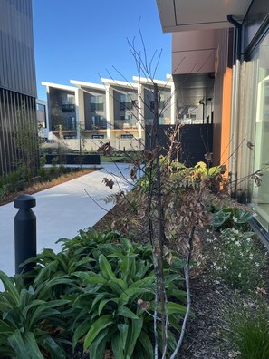 Een modern gebouw met een plat dak, grote ramen en een verzorgde tuin met diverse planten.