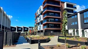 A modern multi-story residential building with balconies, a central pathway, and landscaped areas with small trees. - Inner City Apartment - Prime location! (Christchurch)