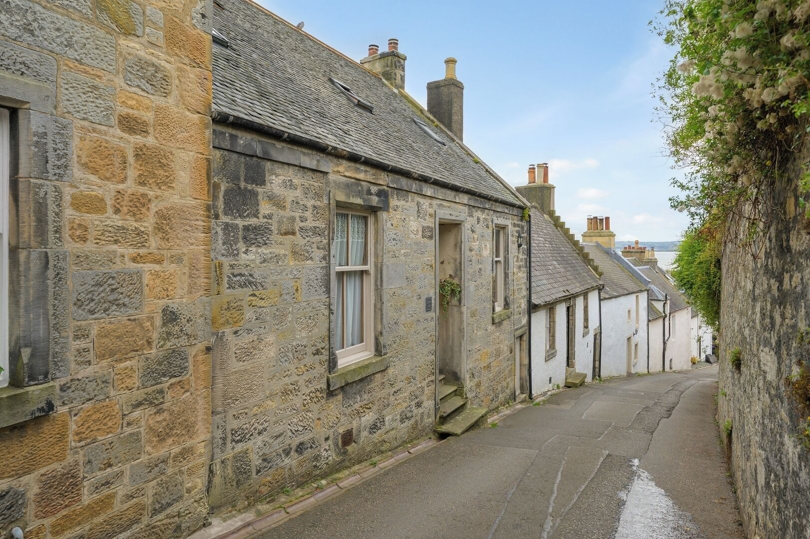 A narrow street lined with stone buildings, some with visible chimneys and windows, suggesting a historic or traditional area.