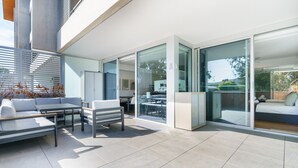 A modern outdoor patio with a sofa, table, and chairs, glass doors leading to a bedroom, and a view of the outdoors. - Quiet Modern Apartment in Prime Location (Reid)