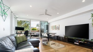 A modern living room with a leather sofa, a glass coffee table, a flat-screen TV, and a dining area with chairs and a table. - Quiet Modern Apartment in Prime Location (Reid)