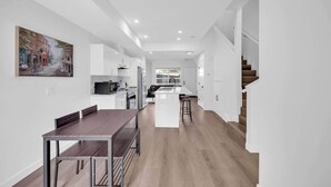 Eine moderne Küche mit weißen Schränken, ein Essbereich mit Holztisch und Stühlen sowie eine Treppe, die in einen weiteren Bereich führt.