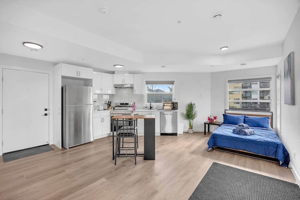 Un apartamento moderno con kitchenette, comedor, cama y un amplio ventanal.