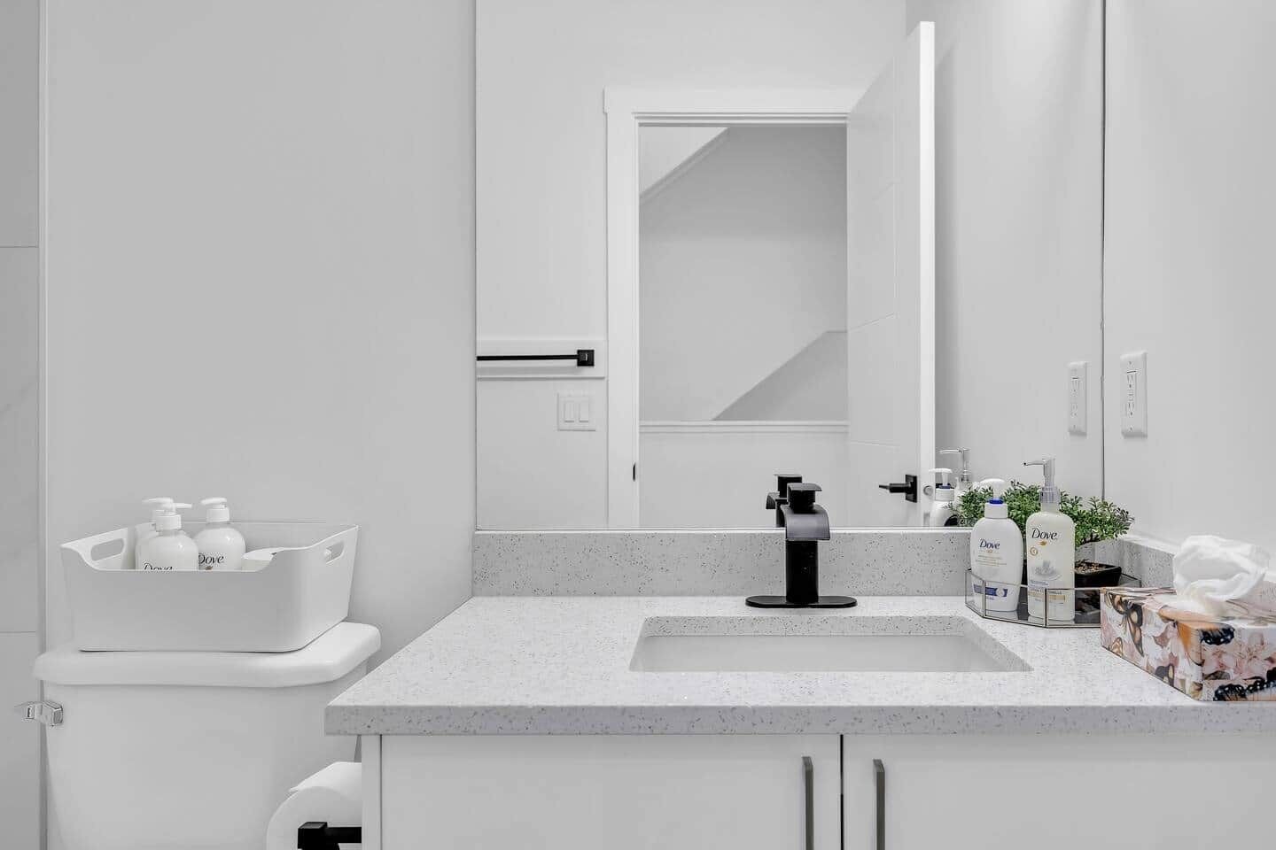 Ett modernt badrum med en vit tvättställ, en spegel och hygienartiklar på bänkskivan.