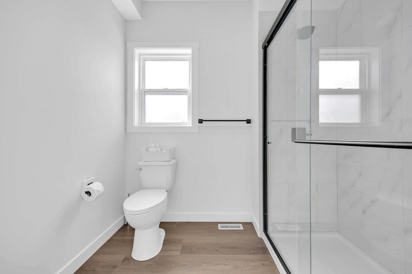 A modern bathroom with a toilet, a window, and a glass shower enclosure.