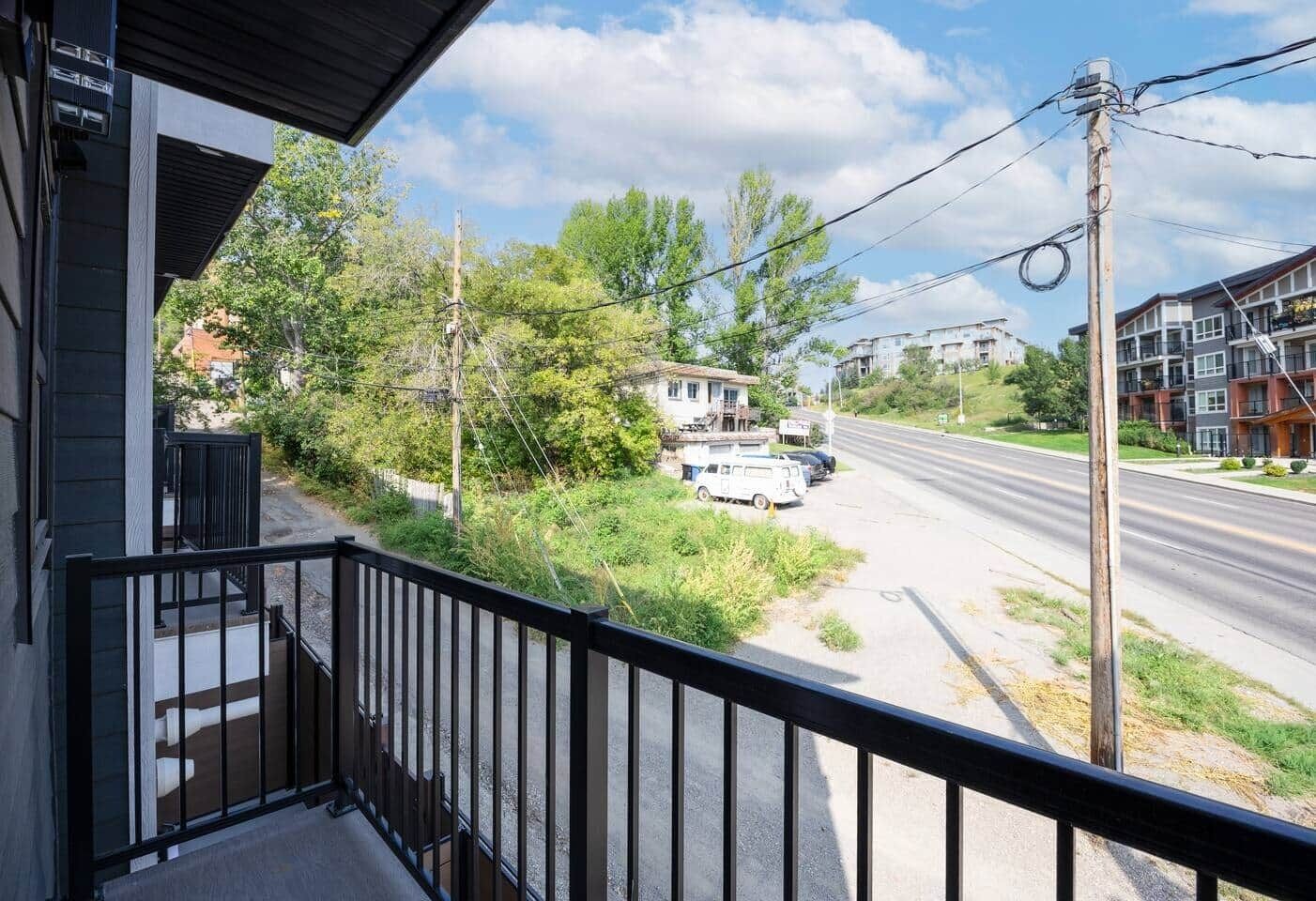 A balcony with a view of a road, parked vehicles, and residential buildings.