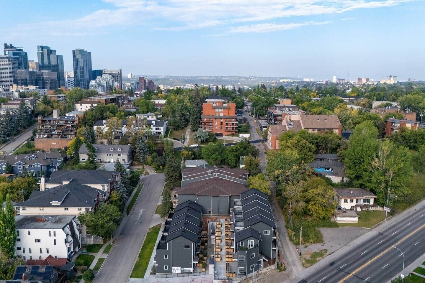Eine Vogelperspektive auf ein Wohngebiet mit modernen Häusern, einer Hauptstraße und einem entfernten Stadtpanorama.