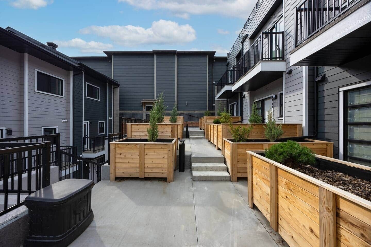Une cour intérieure agrémentée de jardinières en bois, d’un chemin en béton et de bâtiments modernes dotés de balcons.