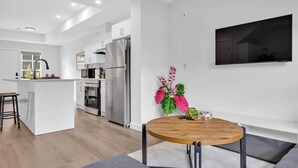 Eine moderne Küche mit Edelstahlgeräten, einem Essbereich mit Holztisch und einem an der Wand montierten Flachbildfernseher.