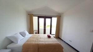 A bedroom with a bed, a small table, and a view of the outdoors through a sliding door. - Rumah WJ Room and Suites (Pecatu)