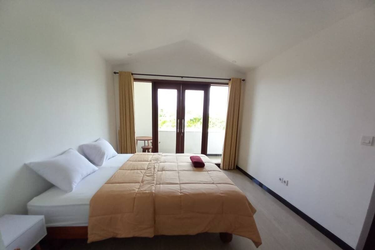 Un dormitorio con cama, una mesita y vistas al exterior a través de una puerta corredera.