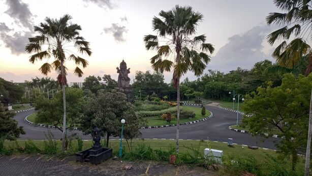 A landscaped area with palm trees, a statue, and a roundabout. - Rumah WJ Room and Suites (Pecatu)