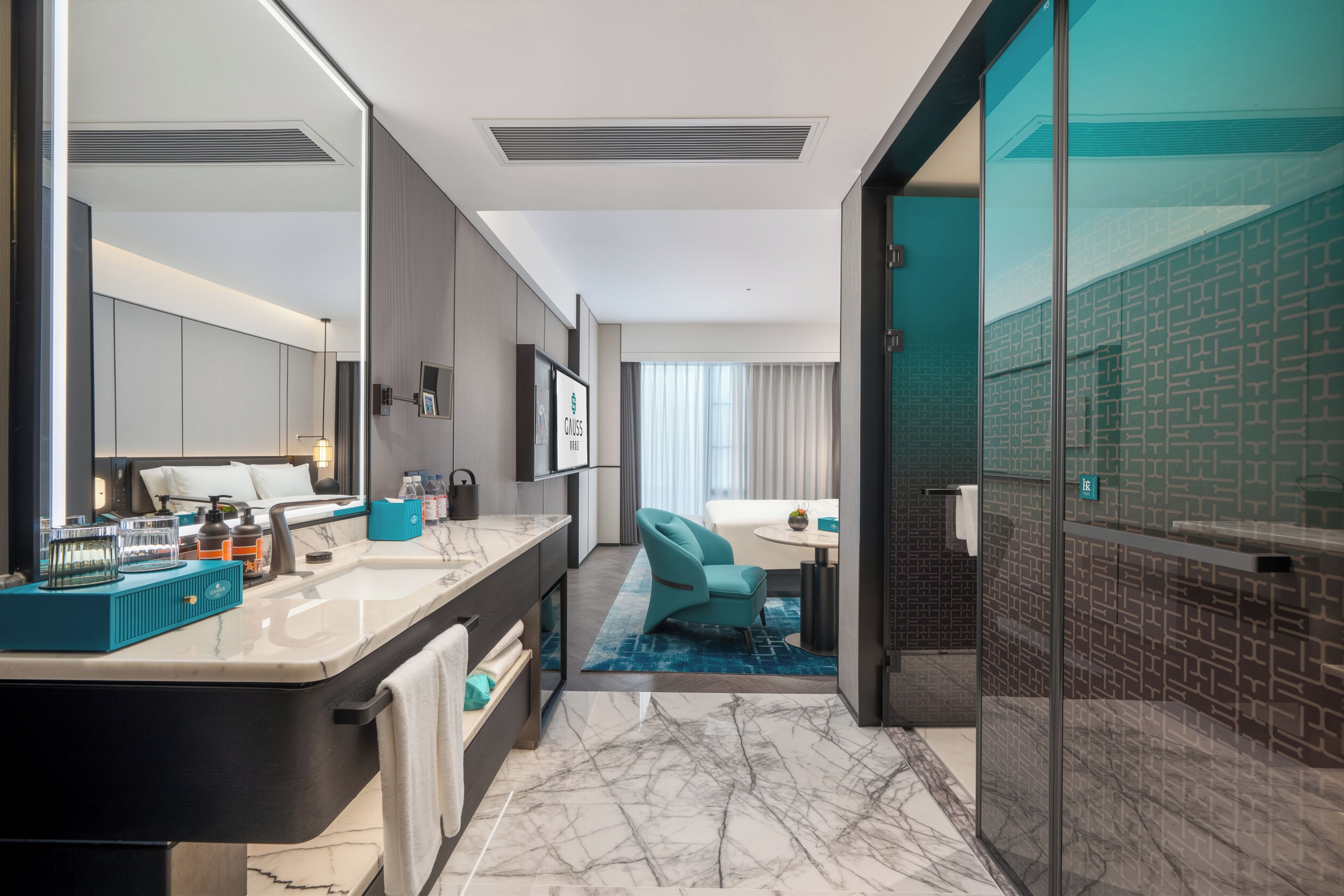 Un baño de hotel moderno con un espejo grande, un tocador con encimera de mármol y una zona de ducha con puerta de cristal.