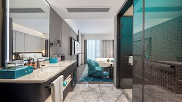 Un baño de hotel moderno con un espejo grande, un tocador con encimera de mármol y una zona de ducha con puerta de cristal.