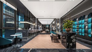A modern hotel lobby with a long reception desk, seating area, and a large potted plant.