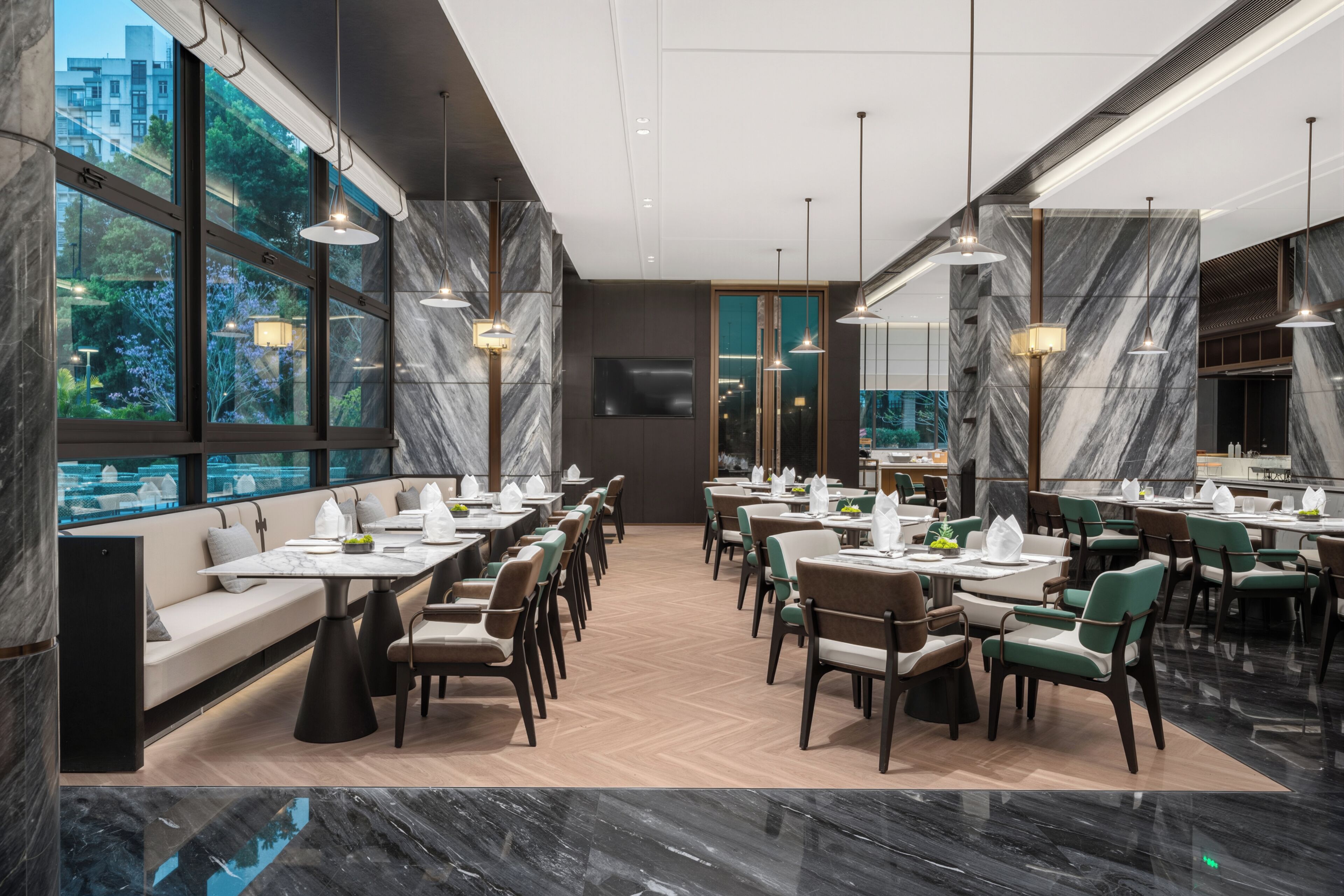 A modern restaurant with marble walls, large windows, and a variety of seating arrangements.
