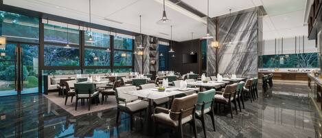 A modern restaurant with marble flooring, large windows, and a variety of seating arrangements.