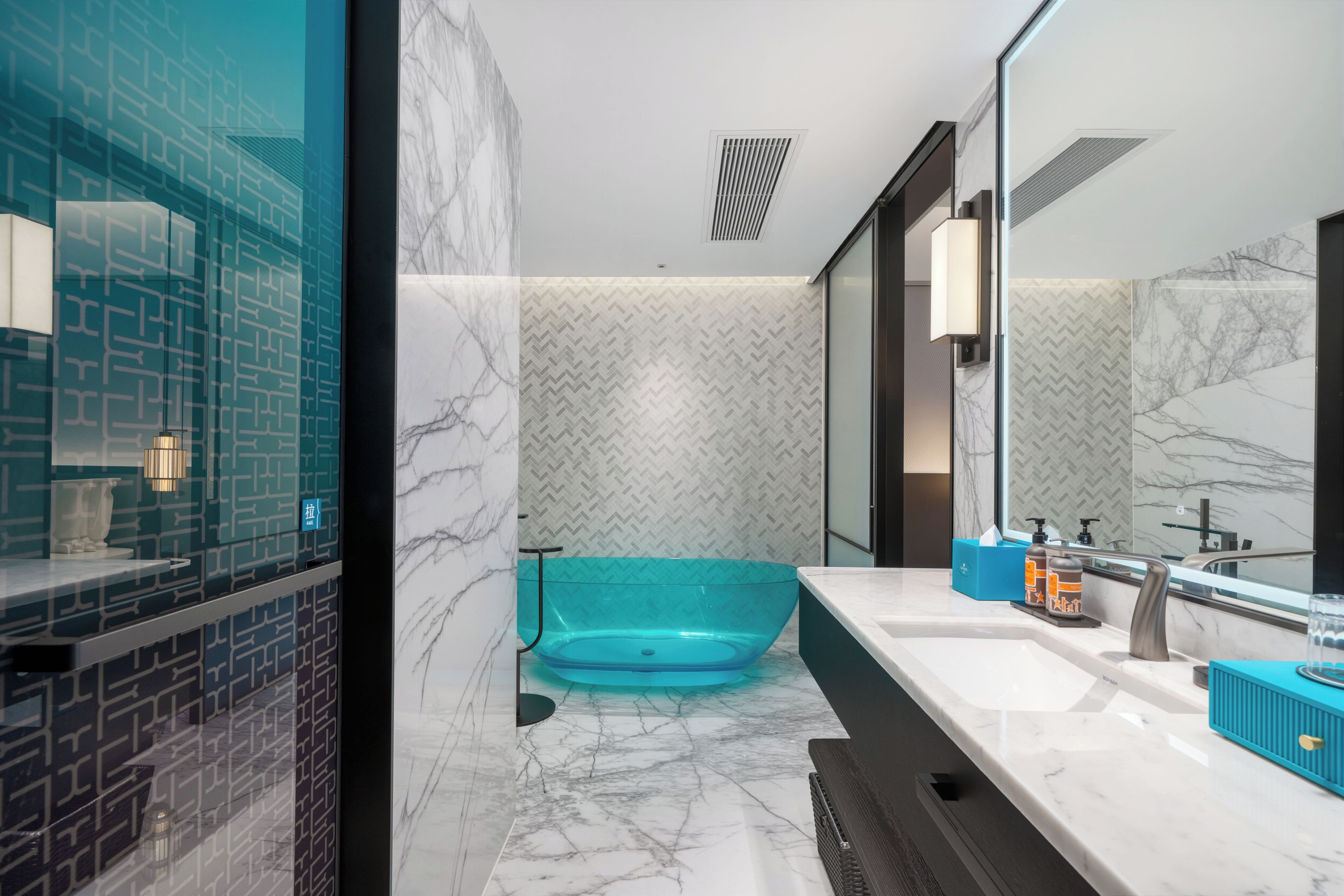 A modern bathroom with a marble floor, a glass bathtub, and a large mirror.