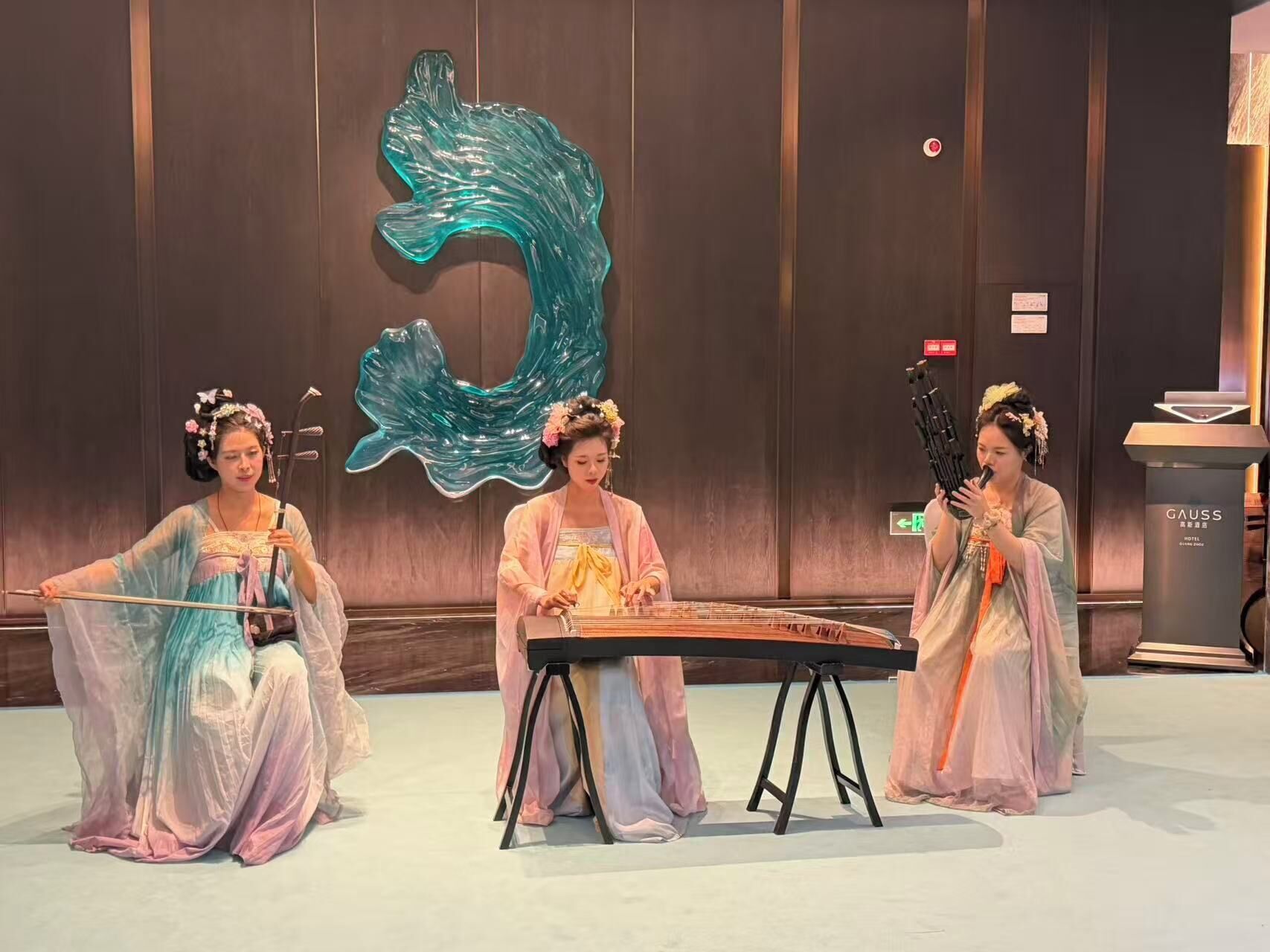 Trois personnes, vêtues de costumes traditionnels, se produisent sur une scène devant un grand panneau décoratif.