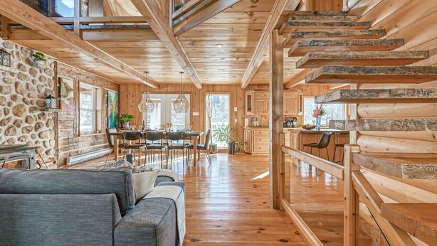 Interior espaçoso de uma cabana de toras, com área de refeições, cozinha e escada.