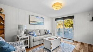 Ein Wohnzimmer mit einer Couch, einem Couchtisch, einem Beistelltisch und einer Lampe. Ein großes Fenster bietet einen Blick ins Freie.