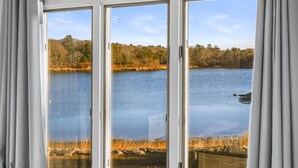 Blick durch Glastüren auf einen See mit Bäumen und blauem Himmel.