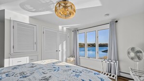 Ein Schlafzimmer mit einem großen Bett, Seeblick, Deckenventilator und einem Fenster mit Vorhängen.