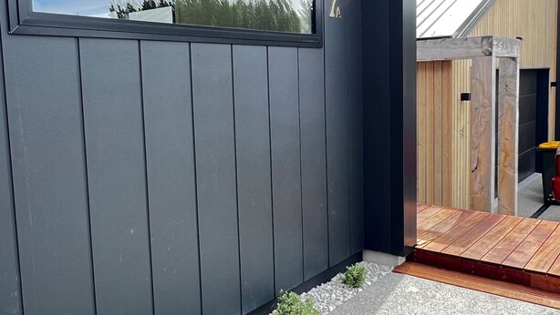 A modern building with a dark facade, a large window reflecting trees, and a wooden deck. - Lovely one-bedroom apartment with AC and stunning mountain views in Jacks Point (Jack's Point)
