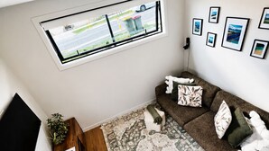 A modern living room with a large window, a flat-screen TV, a sofa set, a patterned rug, and a wooden sideboard with plants. - Lovely one-bedroom apartment with AC and stunning mountain views in Jacks Point (Jack's Point)