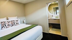 A hotel room with a bed, a bathroom with a mirror, and a view of the outside. - Lovely one-bedroom apartment with AC and stunning mountain views in Jacks Point (Jack's Point)