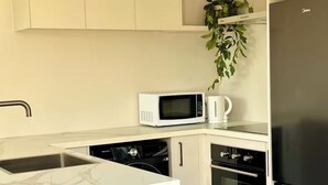 A modern kitchen with white cabinetry, a built-in microwave, a coffee machine, a dishwasher, and a refrigerator. - Lovely one-bedroom apartment with AC and stunning mountain views in Jacks Point (Jack's Point)