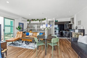 A modern living room with a leather sofa, a dining table with chairs, a coffee table, and a large window. - Sleek 1 Bedroom Wharf-Side Urban Retreat (Auckland City)