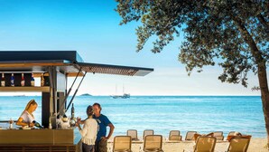 Eine Strandbar mit Blick aufs Meer, mehreren Liegestühlen und einem Schiff in der Ferne.