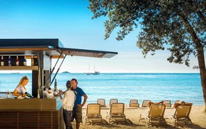 A beachside bar with a view of the sea, several lounge chairs, and a ship in the distance. - Holiday apartment with terrace (Rovinj)