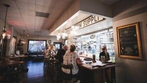 Un espace bar avec un panneau bien visible indiquant « FOURNITURES », des tabourets de bar et un menu écrit à la craie.