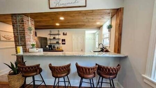 Une cuisine avec un plafond en bois, un coin bar avec des tabourets et une enseigne indiquant « Fait à la main ».