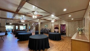 A spacious hall with multiple round tables, wooden flooring, and ceiling fans. - Spacious Lodge Retreat | Sleeps 24 | 8 Suites | Decks, Pond Views & Gathering Spaces (Zwolle)