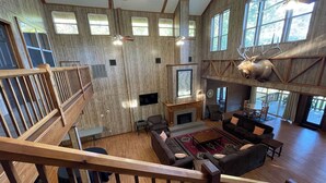 A spacious interior with a fireplace, multiple seating areas, and large windows. - Spacious Lodge Retreat | Sleeps 24 | 8 Suites | Decks, Pond Views & Gathering Spaces (Zwolle)