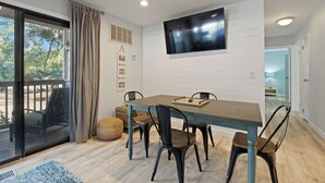 A dining area with a table and chairs, a television mounted on the wall, and a view of the outdoors through a sliding door. - Fully renovated 2BR/2BA within walking distance to the beach and so much to do! (Hilton Head Island)