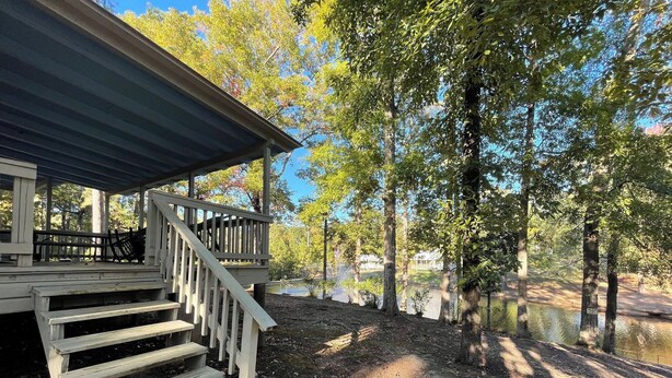 A wooden deck with steps leading to a covered porch, surrounded by trees and a body of water. - Comfortable 3-Bedroom Retreat with Fireplace, Full Kitchen & Outdoor Firepit (Zwolle)