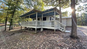A cabin with a covered porch, surrounded by trees and a dirt ground. - Comfortable 3-Bedroom Retreat with Fireplace, Full Kitchen & Outdoor Firepit (Zwolle)