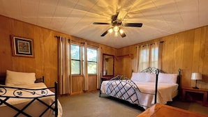 Une chambre avec deux lits, un plancher en bois, un ventilateur de plafond et une fenêtre avec des rideaux.