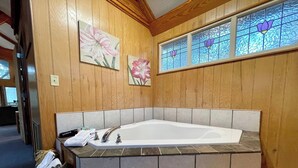 Un baño con una bañera grande, paneles de madera y un ventanal de vidrio emplomado.
