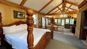 Un dormitorio con estructura de madera, una cama grande, un área de comedor y vistas al exterior.