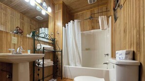 A wooden-paneled bathroom with a sink, toilet, and bathtub. - Peaceful Cabin with Full Kitchen, Vaulted Ceilings & Pond View Porch (Zwolle)