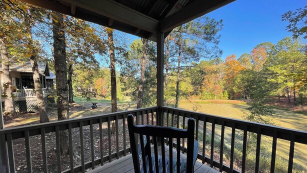 A covered porch with a wooden bench, overlooking a grassy area with trees and a building in the background. - Peaceful Cabin with Full Kitchen, Vaulted Ceilings & Pond View Porch (Zwolle)