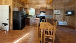 A wooden cabin interior with a kitchen, dining area, and a door. - Vaulted-Ceiling Cabin for 4 with King Bed + Bunks, Full Kitchen & Pond Views (Zwolle)